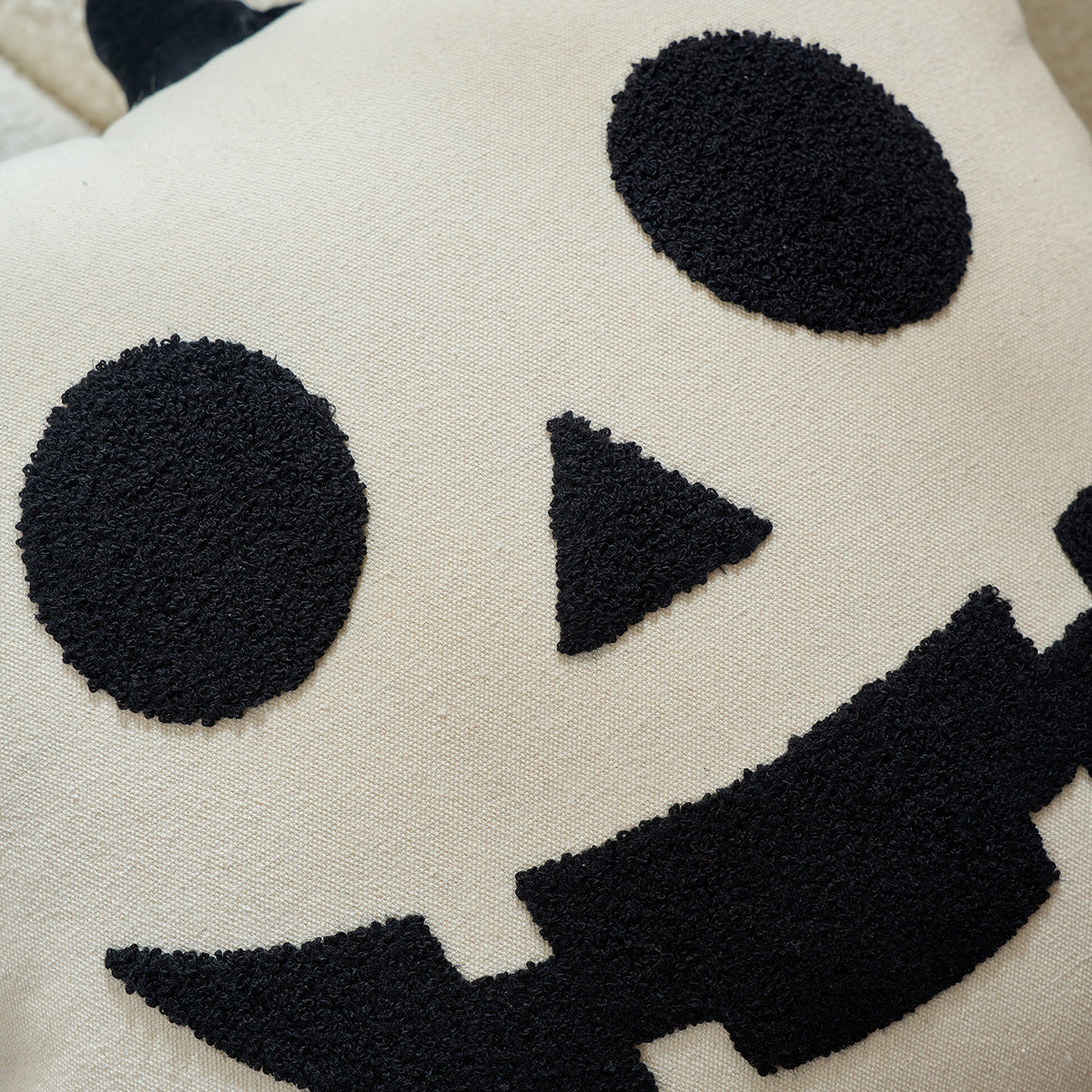 Close-up of the tufted ghost face embroidery on a cream cushion